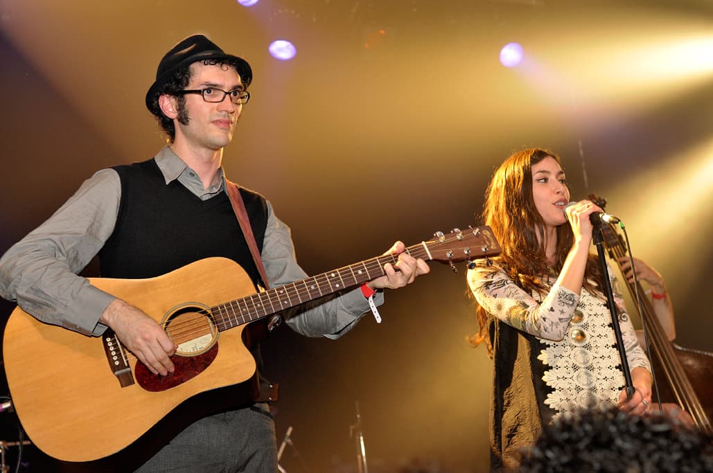 Guitariste à chapeau et lunettes accompagnant une chanteuse rousse au micro