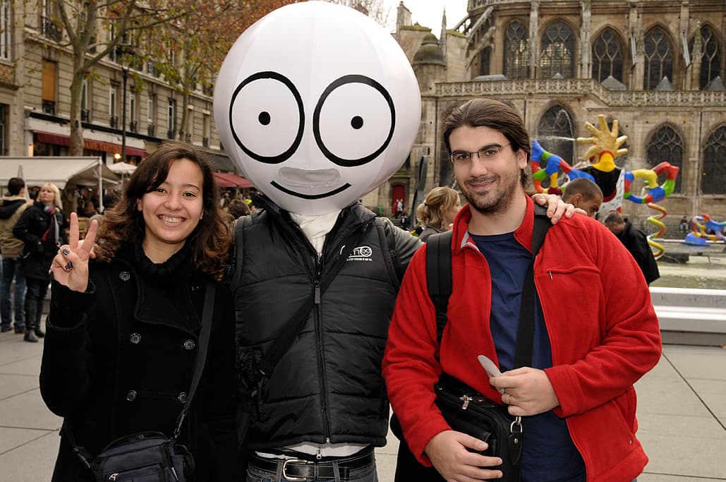 Mascotte à grosse tête souriante entre deux passants, opération street marketing à Paris