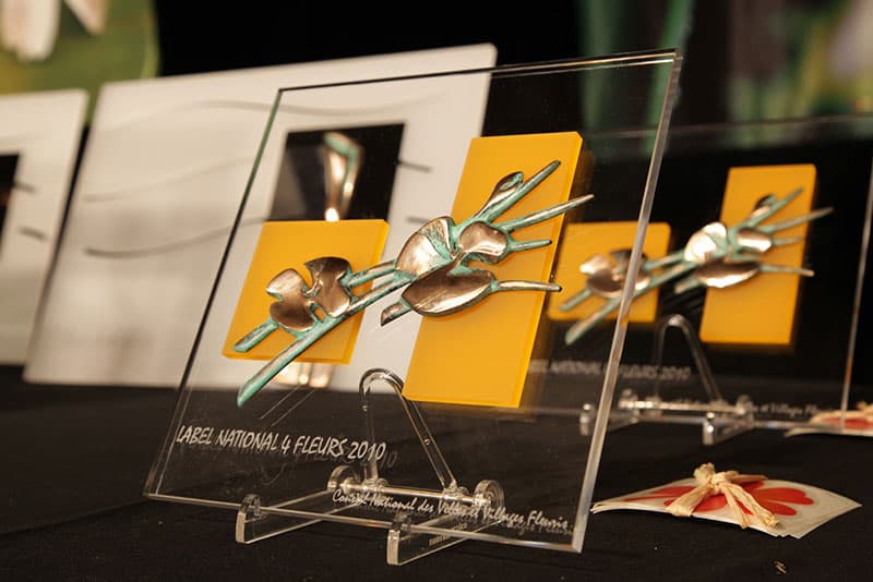 Trophées Label National 4 Fleurs 2010 en verre et bronze alignés sur une table