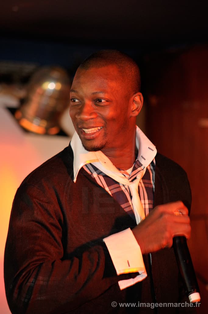 Chanteur souriant en gilet sombre tenant un micro, lumière orangée